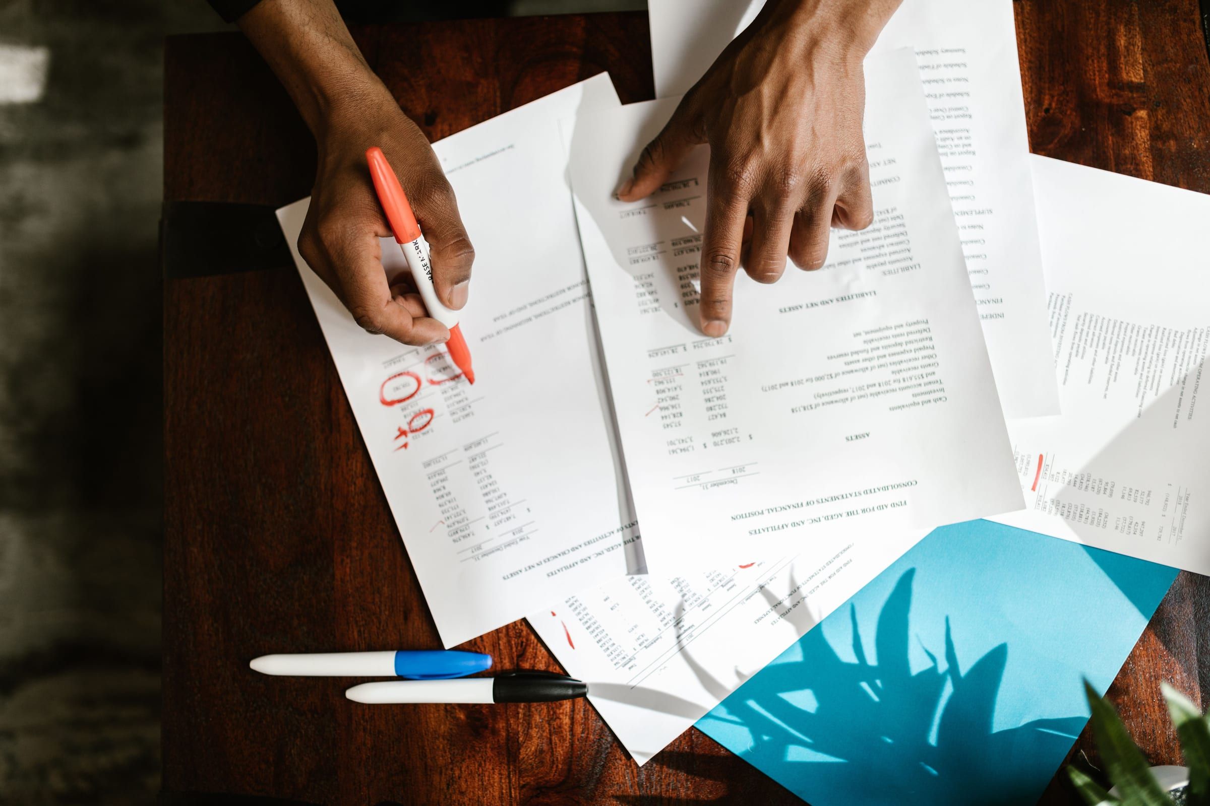 Hands marking figures on a statement of financial position with a red pen
