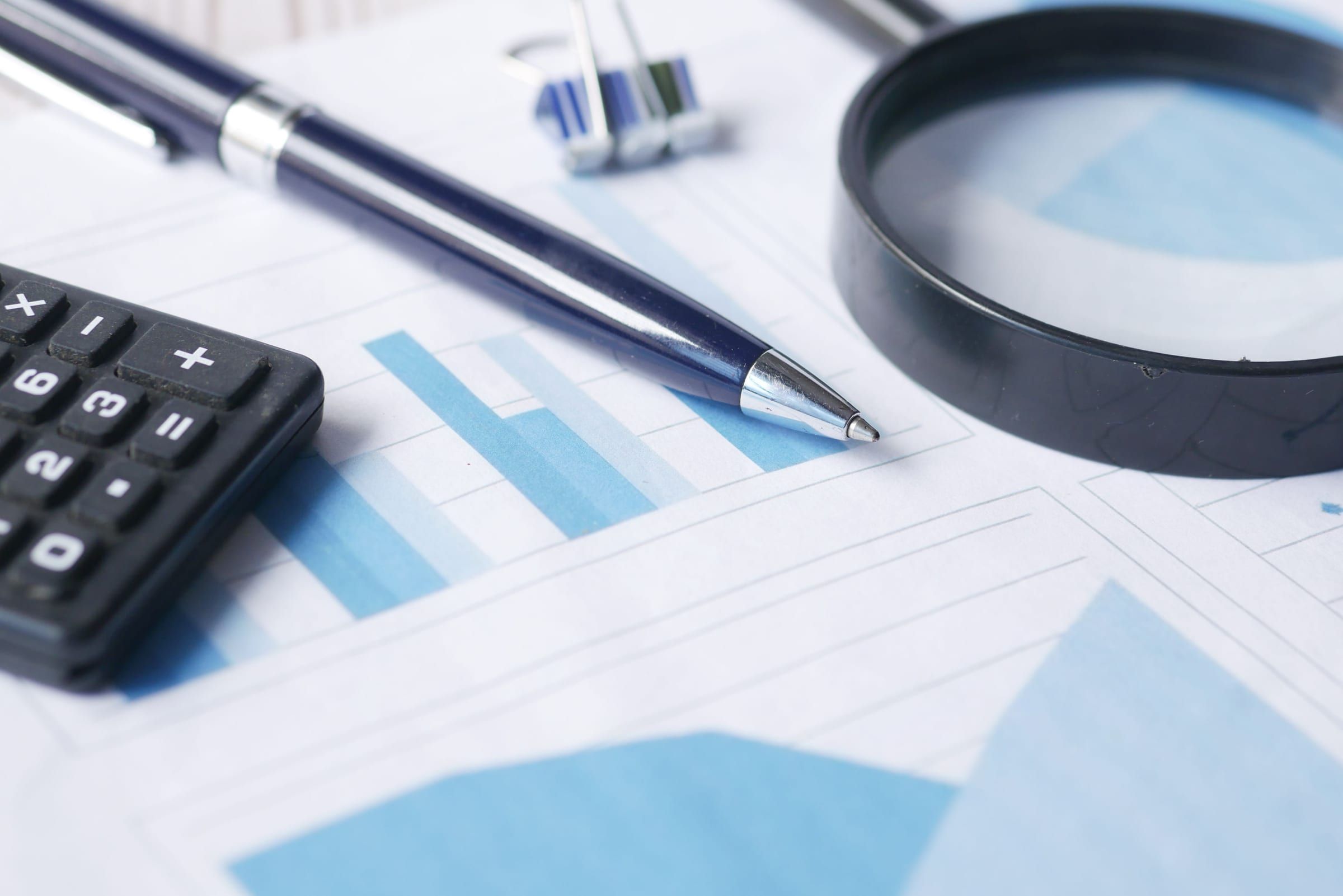 Calculator, pen and magnifying glass resting on printed financial charts